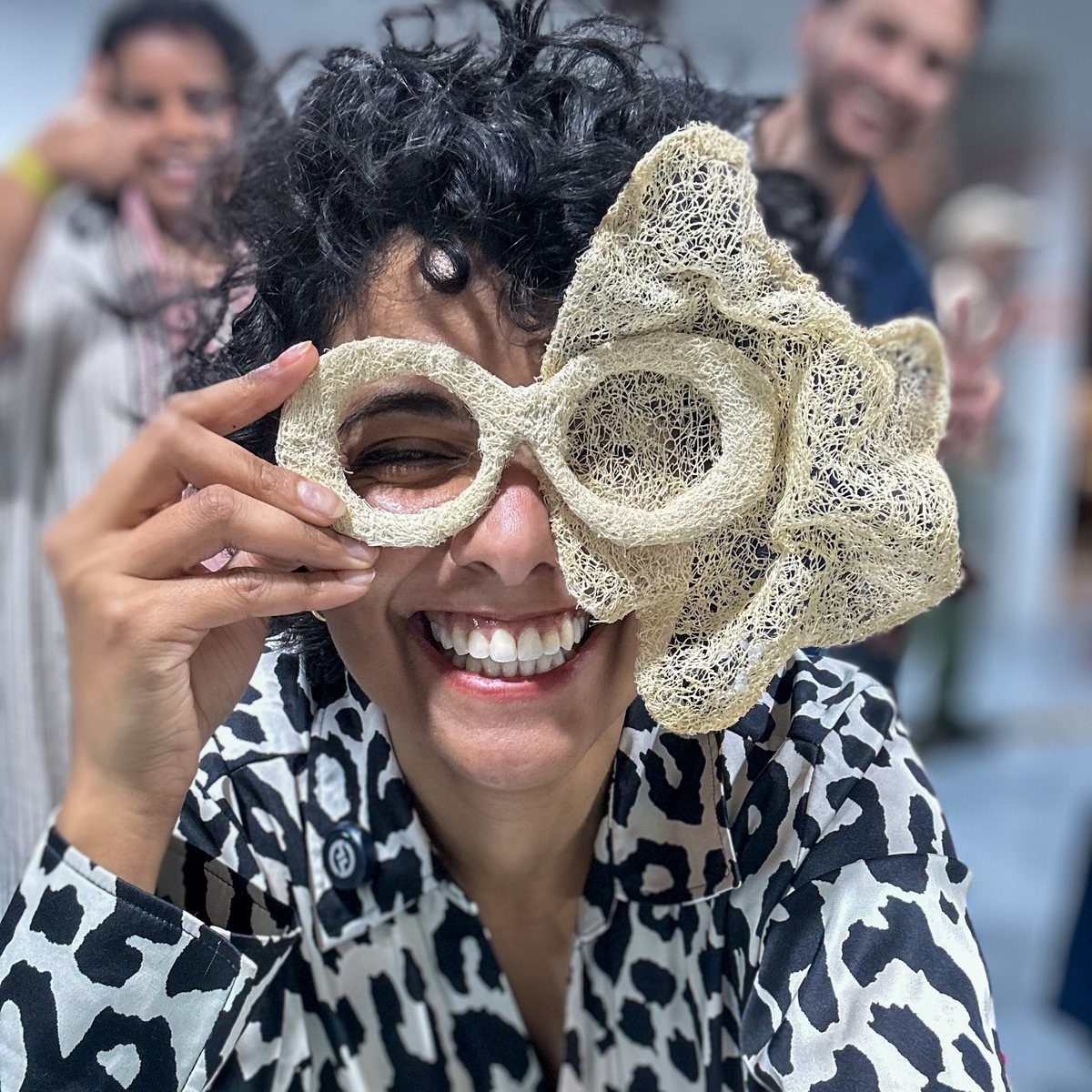 Marya Mayan holding Third Eye in front of her eye among visitors at an exhibition